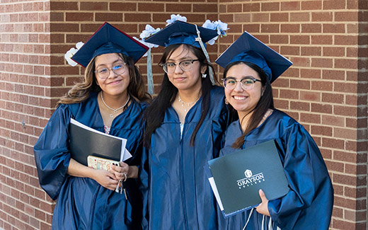 Three graduates posing in front of brick wall