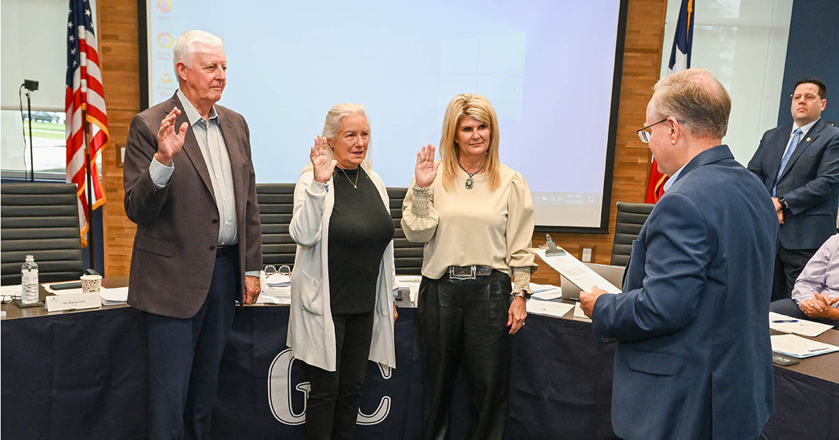 Three board members standing side by side with hands raised while taking oath.